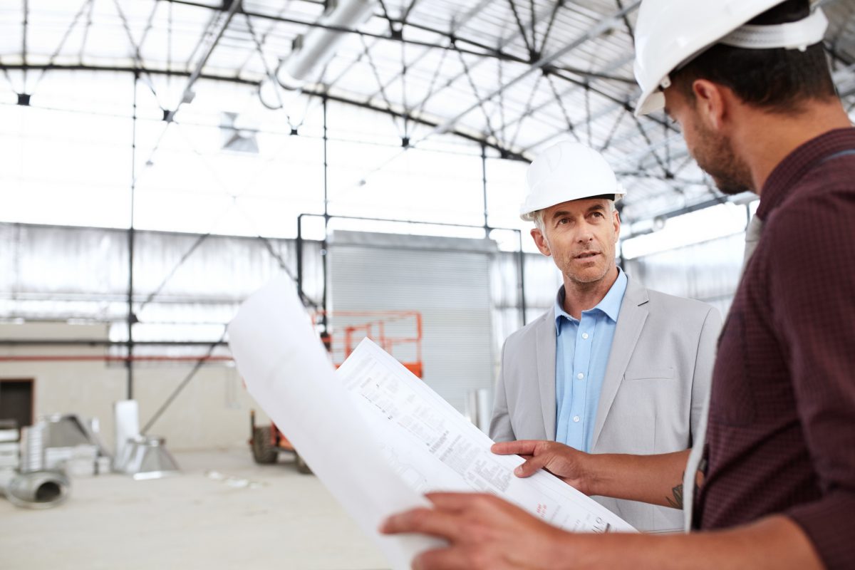 Building Engineers Talking Together Over Blueprints During A Worksite Inspection